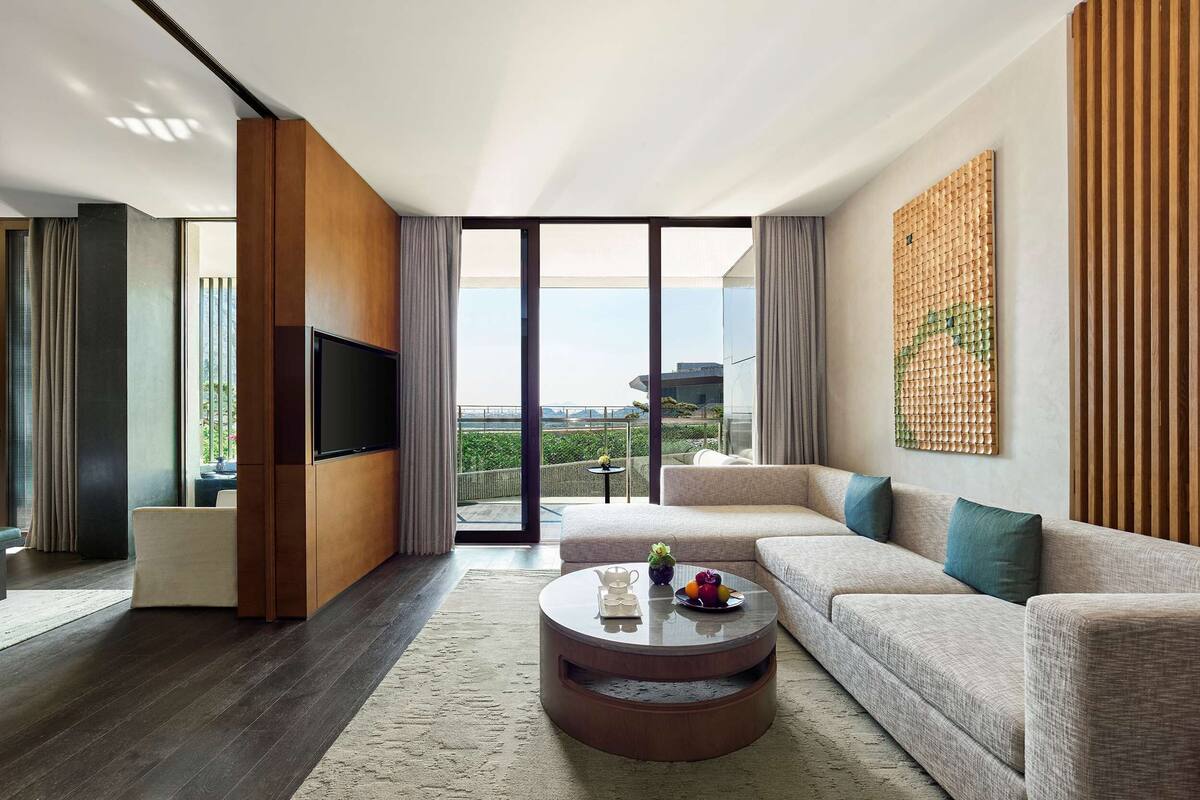 Een moderne woonkamer met een grote flatscreen televisie, een ronde salontafel met fruit, een bank en een groot raam met uitzicht op de stad.