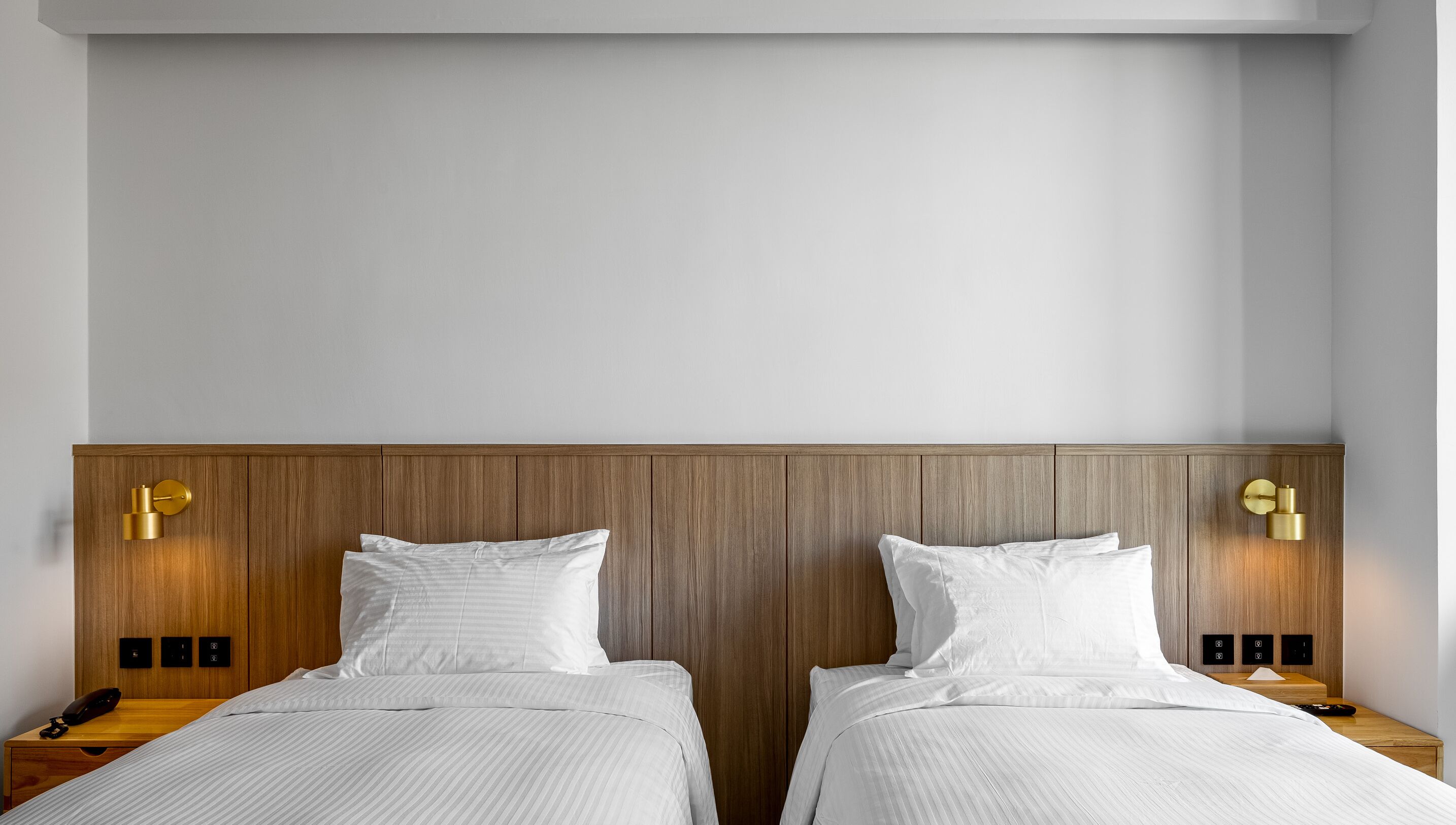 A double room with two beds, wooden headboard, bedside tables, and wall-mounted light fixtures.