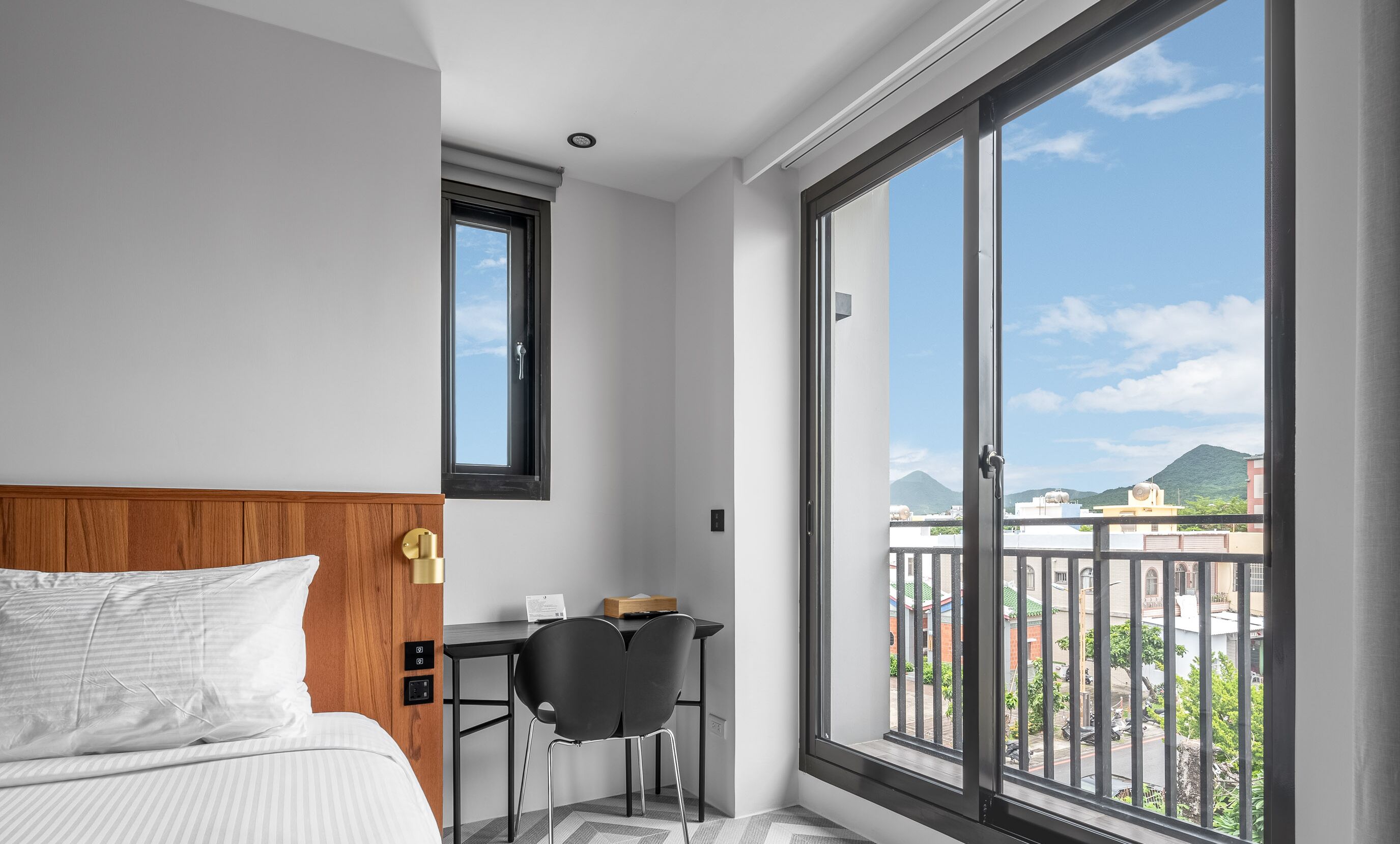 Habitación de hotel con cama, escritorio y un amplio ventanal que ofrece vistas a la ciudad.