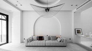 A modern living room with a grey sofa, a unique ceiling light fixture, and a minimalist design. - Black Horn B&B (Hengchun)
