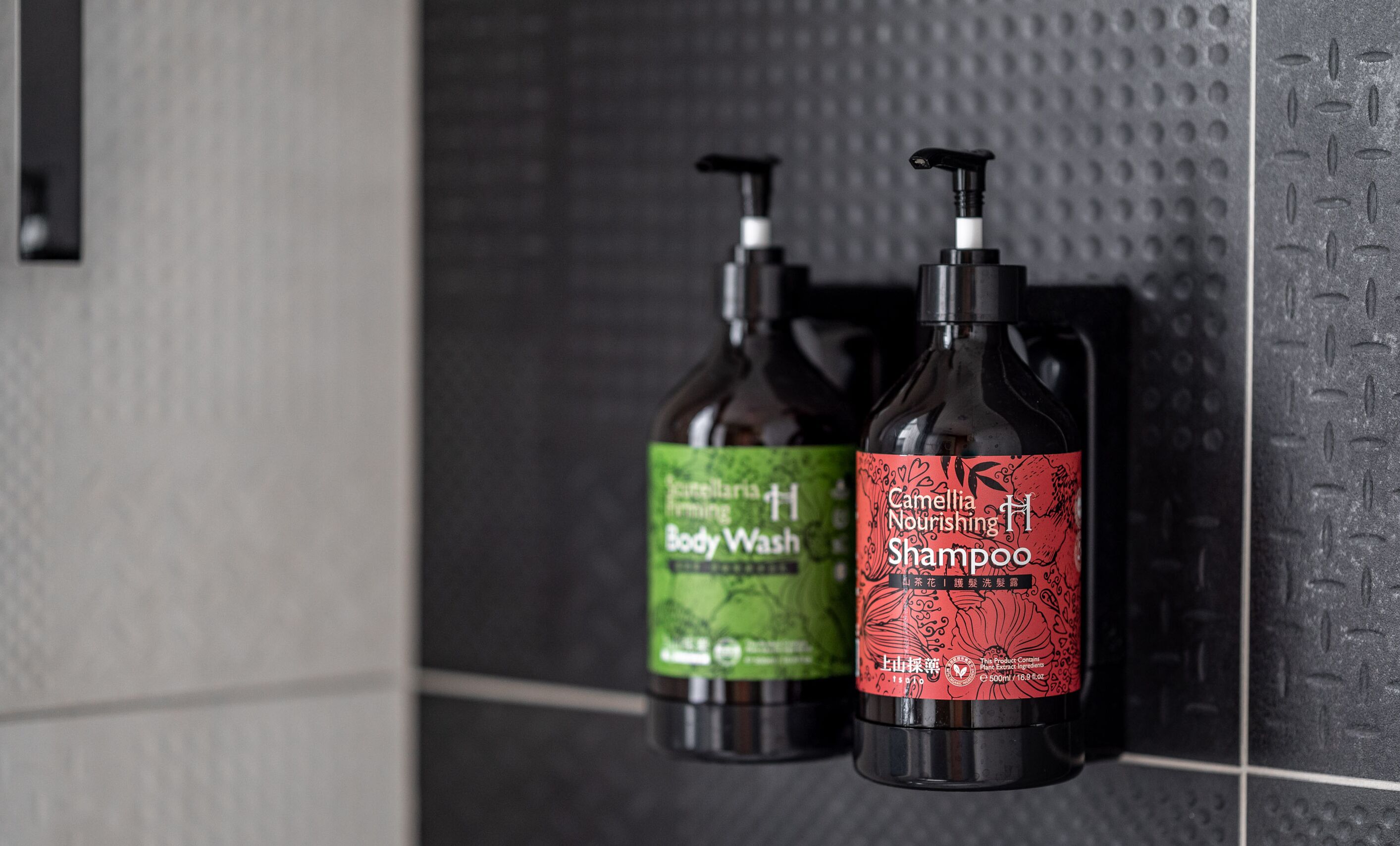 Due flaconi di bagnoschiuma e shampoo su un muro piastrellato.