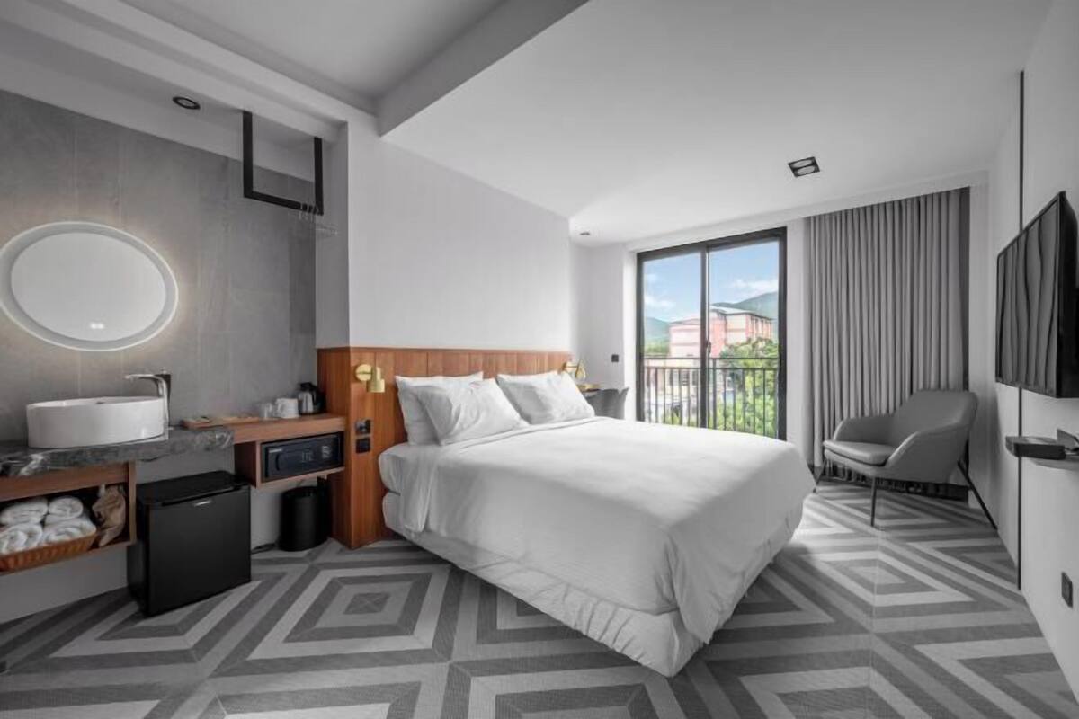 A modern hotel room with a bed, a bathroom, a TV, and a balcony.