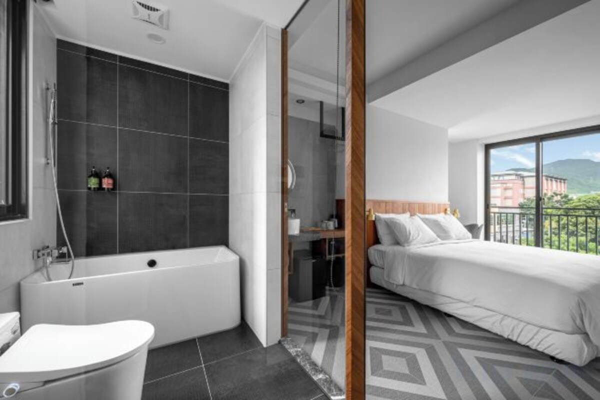 Une chambre d’hôtel moderne dotée d’une baignoire, d’une douche séparée, d’un grand lit et offrant une vue sur l’extérieur.