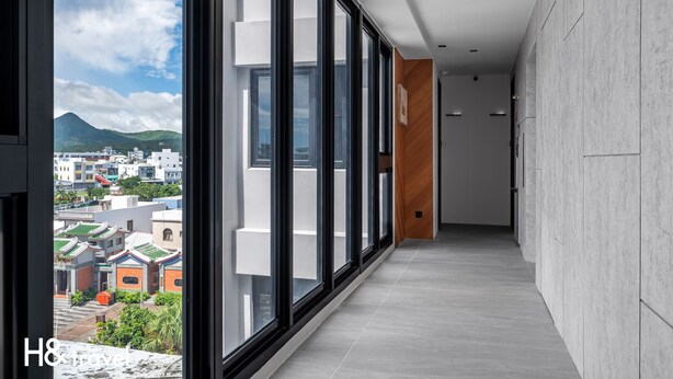 A modern hotel corridor with large windows, a view of traditional buildings, and a wooden accent wall. - Black Horn B&B (Hengchun)