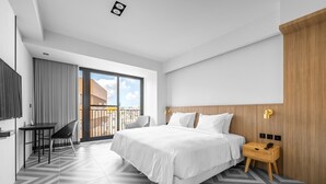 A modern hotel room with a large bed, a desk, a chair, and a view of the city through a balcony. - Black Horn B&B (Hengchun)