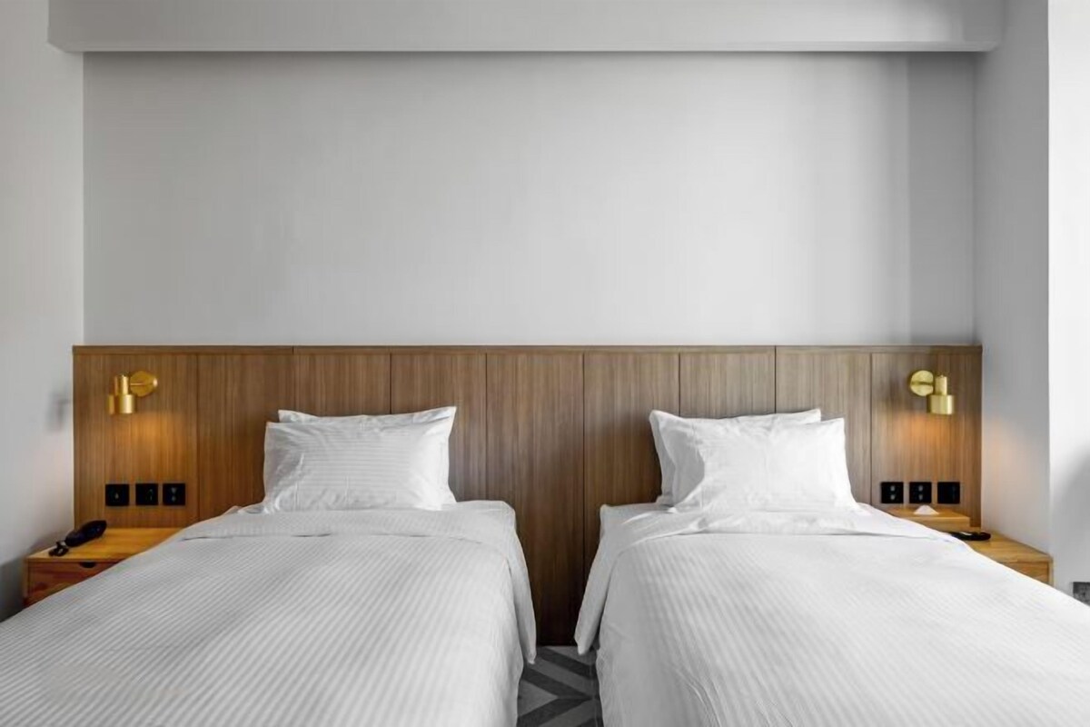 Habitación de hotel con dos camas, cabecero de madera, lámparas de noche y un diseño sencillo y limpio.