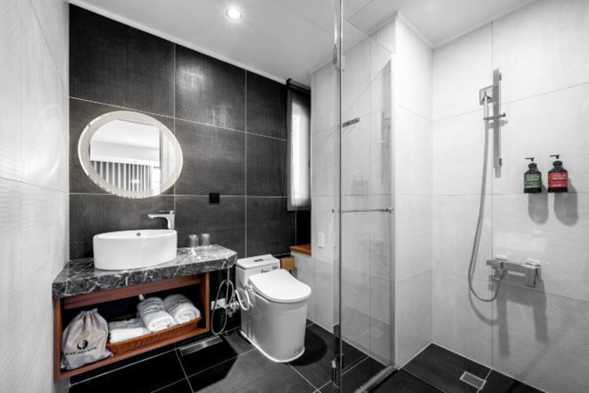 A modern bathroom with a white sink, mirror, and toilet, a glass shower enclosure, and a marble countertop.