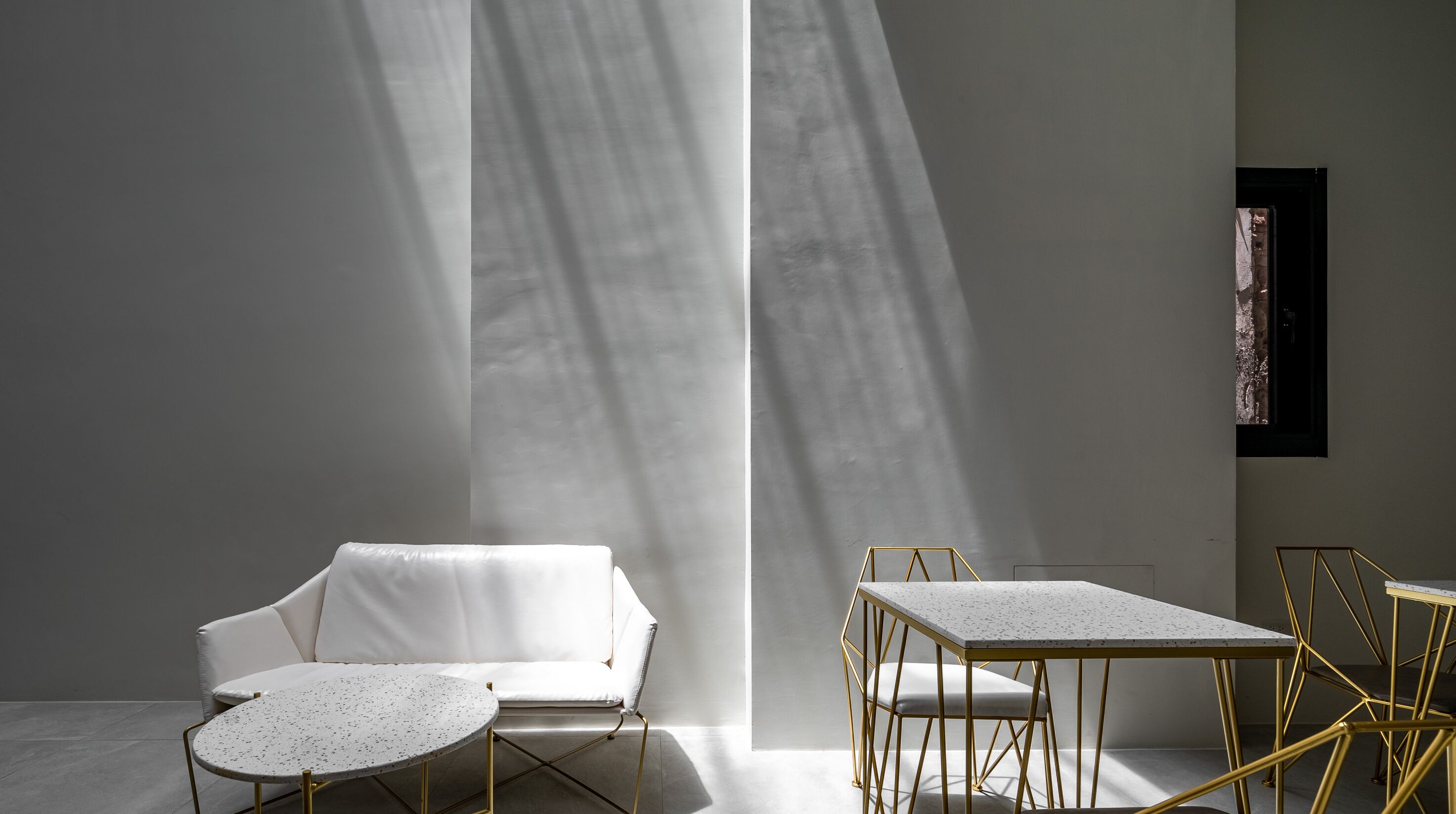 A modern interior with a white sofa, two round tables, and a small dining table with gold frames.