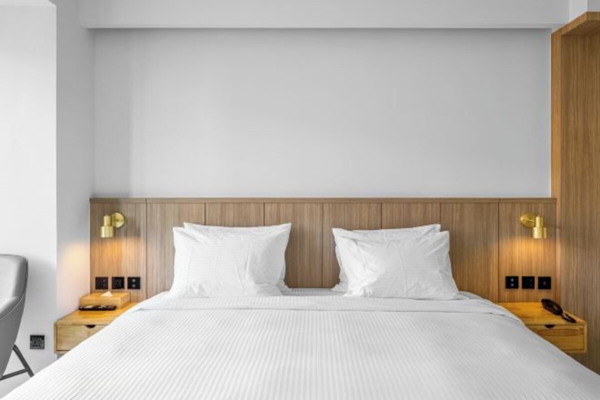 A hotel room with a wooden headboard, two white pillows, a bed with a white bedspread, and two bedside tables with lamps.