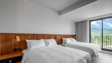 Ett hotellrum med två sängar, en sänggavel i trä, ett stort fönster med utsikt över kullar och en kontrollpanel på vänster sida.