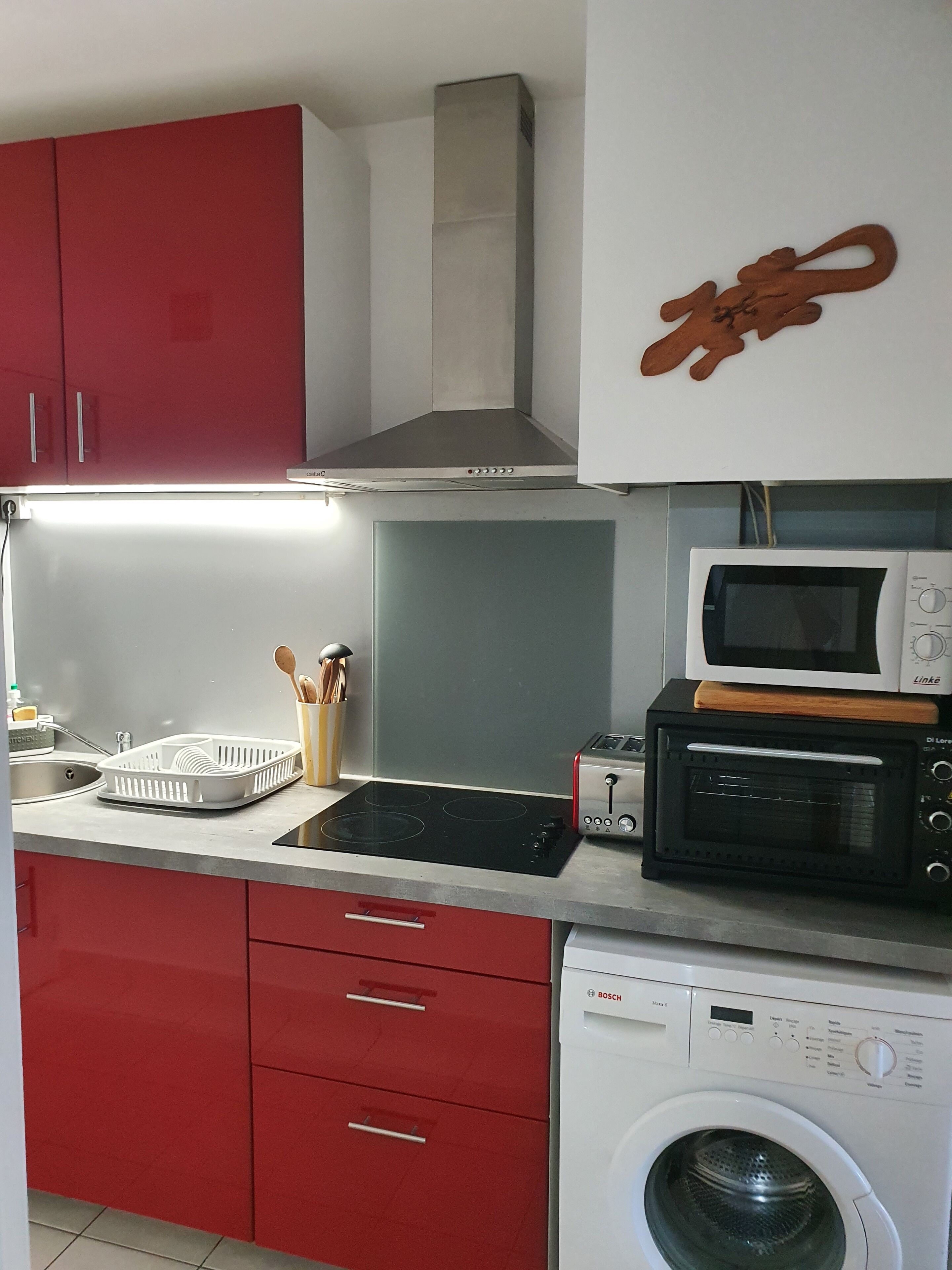Eine kleine Küche mit roten Schränken, einer Mikrowelle, einem Toaster, einer Waschmaschine und einem Spülbecken.