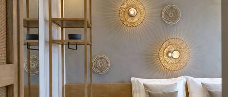 A modern bedroom with a bed, bedside tables, a wooden shelf unit, and decorative wall lights.