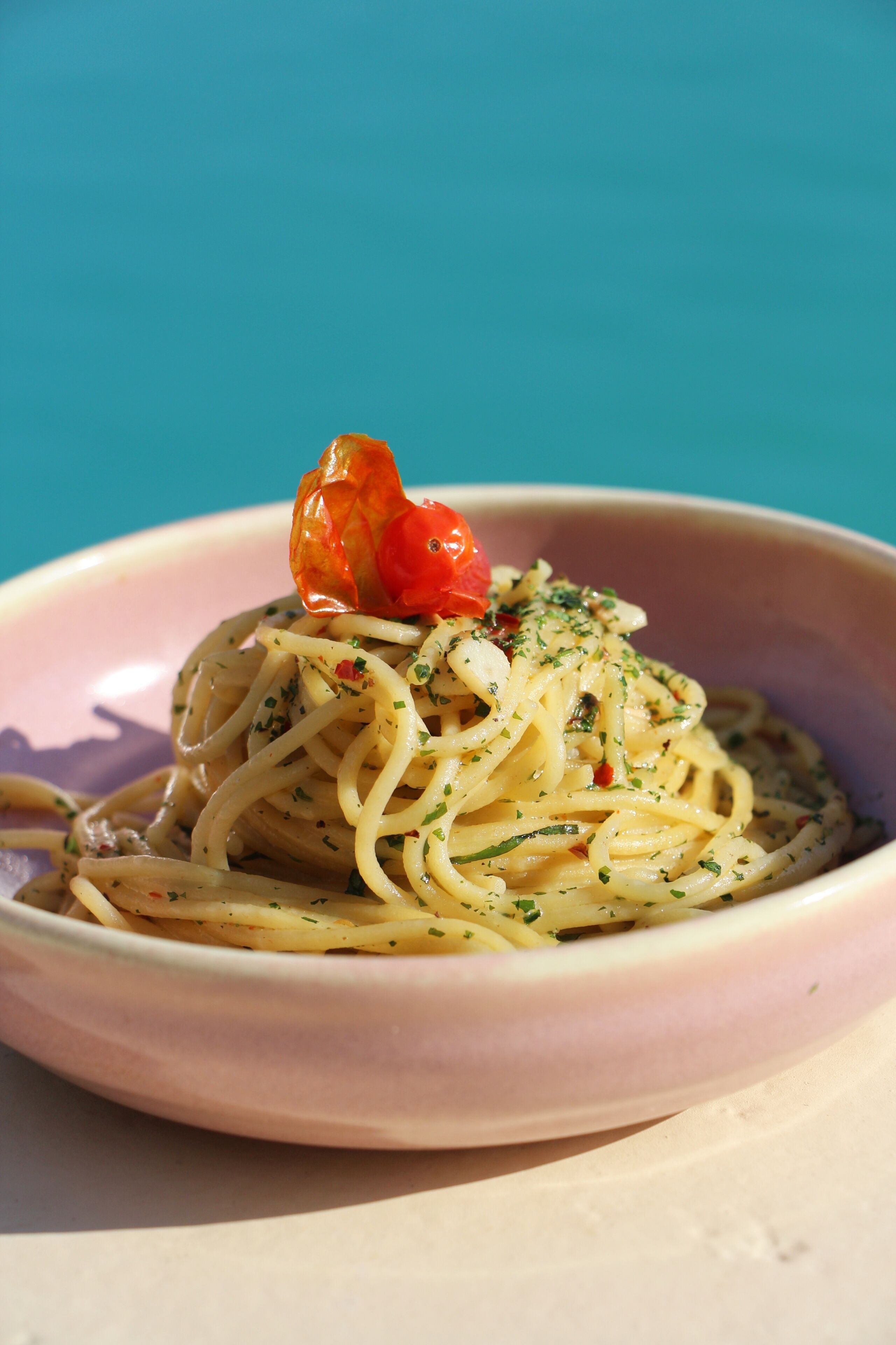 A bowl of spaghetti with a cherry tomato garnish on a table against a blue background.
