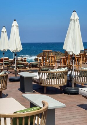 A seaside patio with wooden chairs and tables, white umbrellas, and a view of the ocean. - Bebatroun Beach Hotel (Batroun)