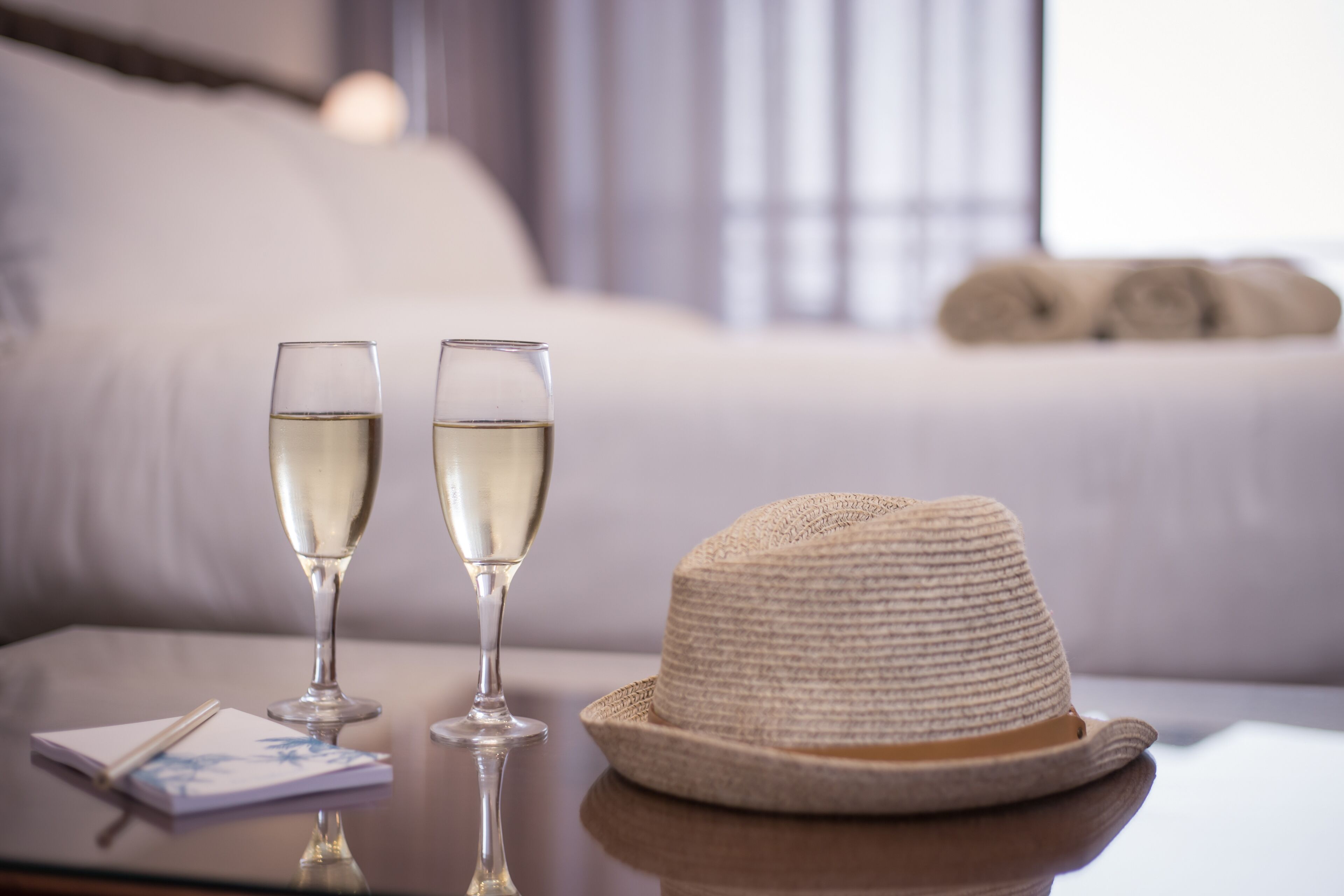 Two glasses of white wine on a table with a straw hat and a notepad.