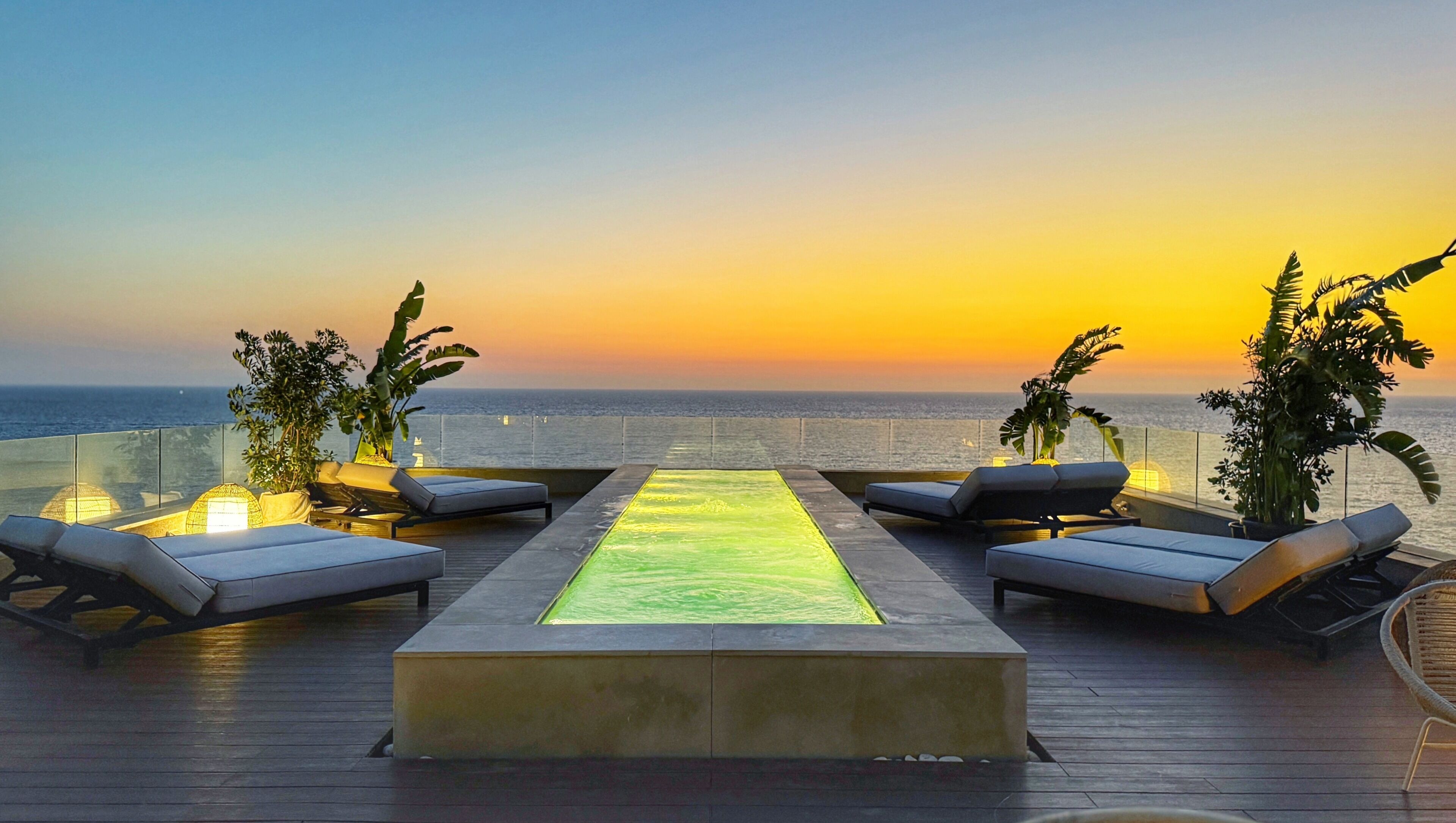A rooftop terrace with a water feature, lounge chairs, and a view of the ocean at sunset.
