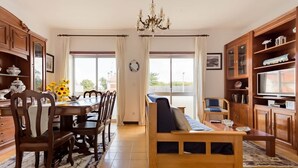 Un salon spacieux comprenant un coin repas, des meubles en bois, un lustre et de grandes fenêtres.