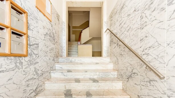 Un escalier en marbre, doté d’une main courante, mène à un palier.
