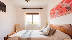 Une chambre à coucher avec un lit, une fenêtre avec des rideaux, une tête de lit en bois et un tableau au mur.