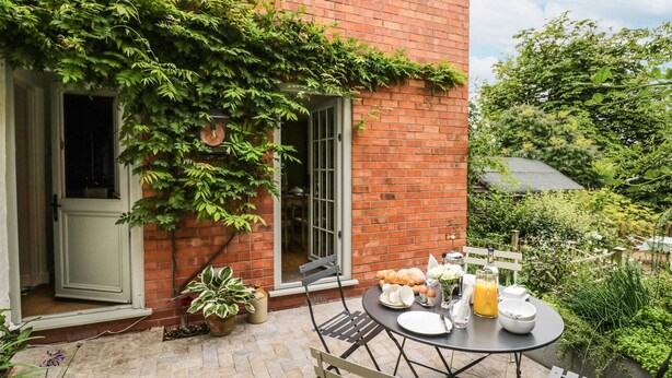 A patio with a table set for breakfast, a brick wall, and greenery.