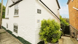 A white brick house with a chimney, a window, and a door. There is a sign on the wall that says "10 Prospect Cottage."