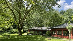 A red building with a tiled roof, surrounded by lush greenery and a well-maintained lawn. - House (Lohmar)