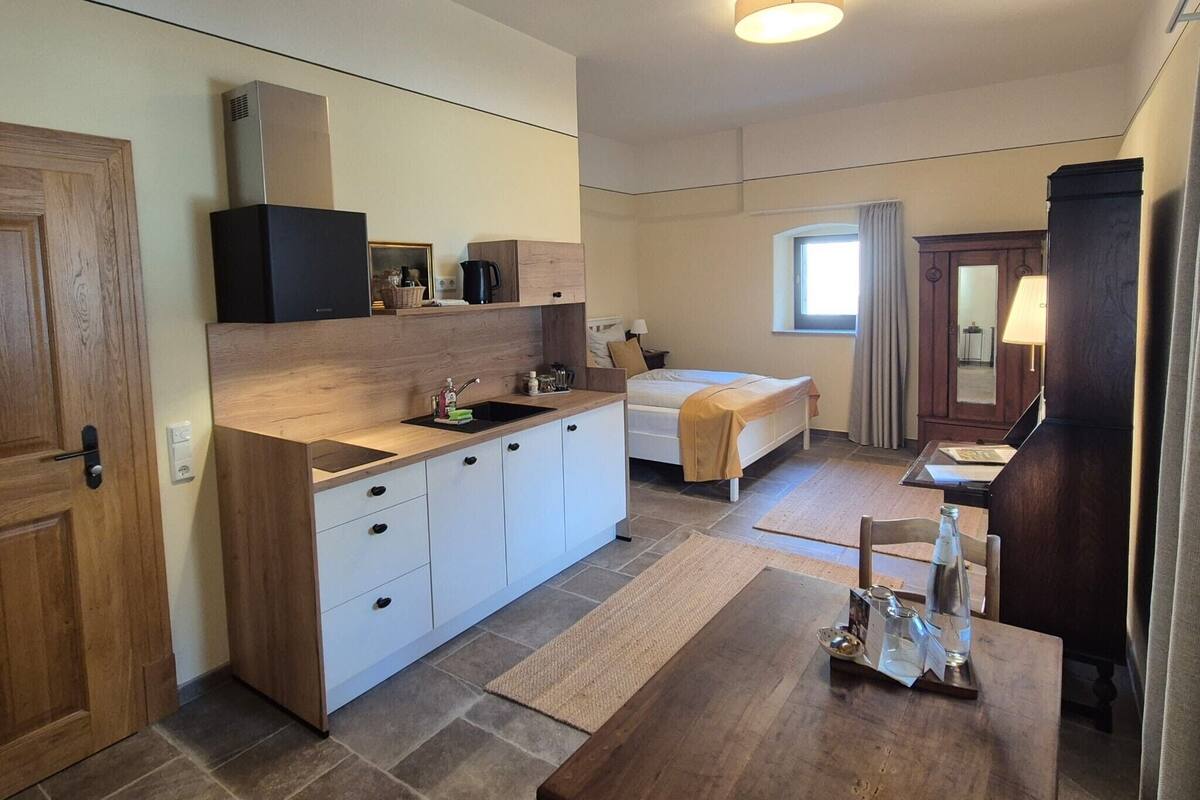 Habitación de hotel pequeña con kitchenette, cama, mesa de comedor y ventana.