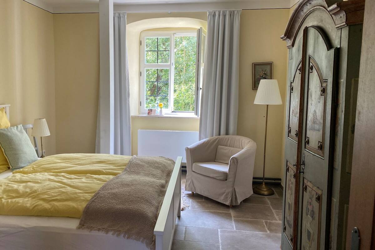 Un dormitorio con una cama, una silla, un ventanal y un armario.