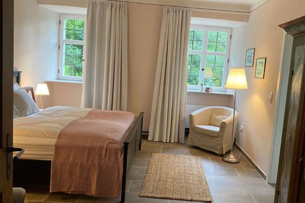 Un dormitorio con cama, una silla, una lámpara y una alfombra.