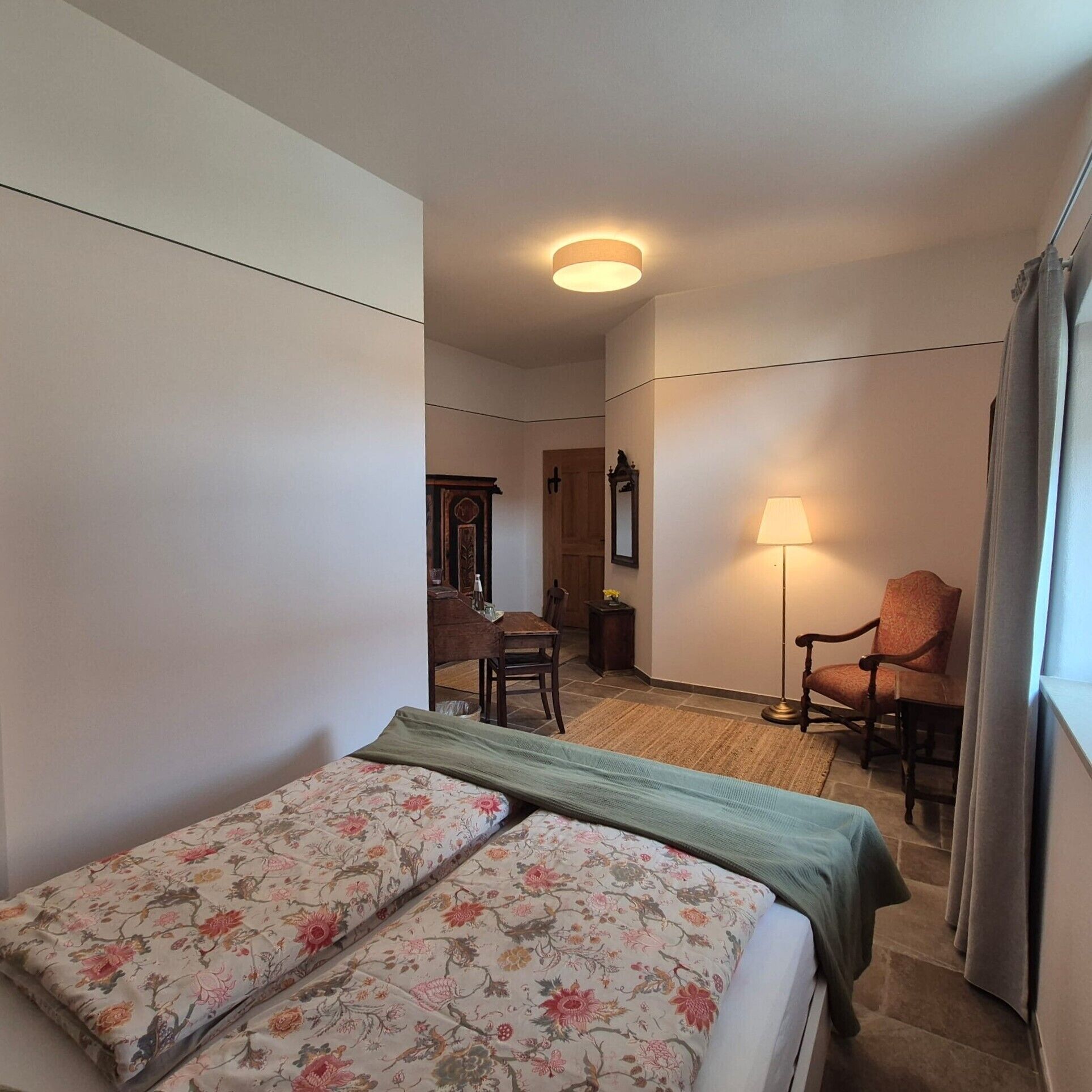 A hotel room with a bed, a chair, a desk, and a lamp.