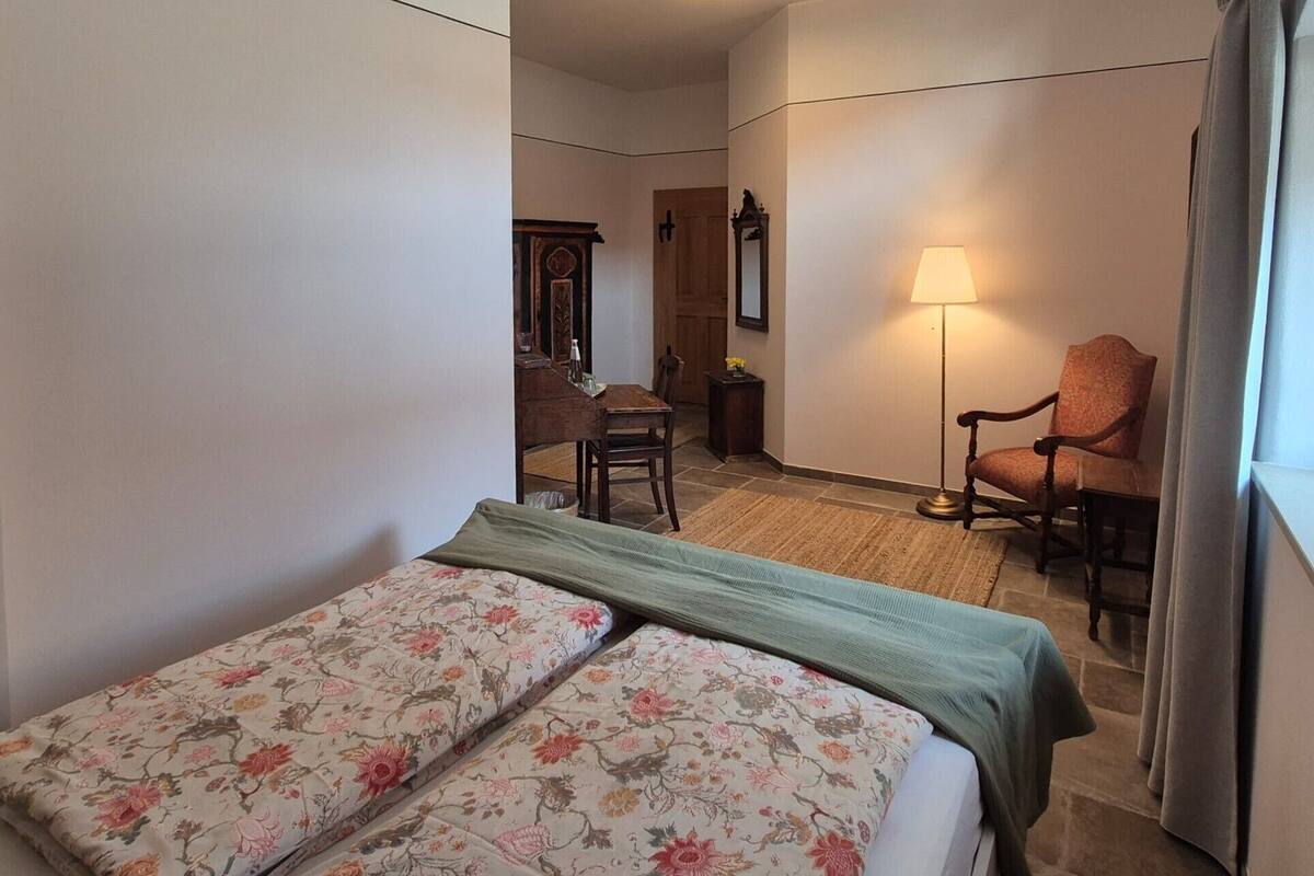 Una habitación de hotel con cama, sillón, escritorio y lámpara.