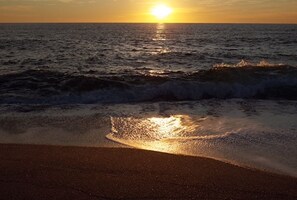 A sunset over the ocean with waves approaching the shore.