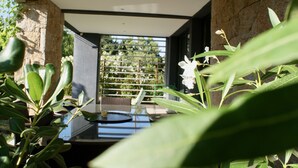 A modern interior with a glass table, stone walls, and a view of greenery outside. - Facing the sea, 30 m from the beach, luxury villa, air-conditioned  (Serra-di-Ferro)