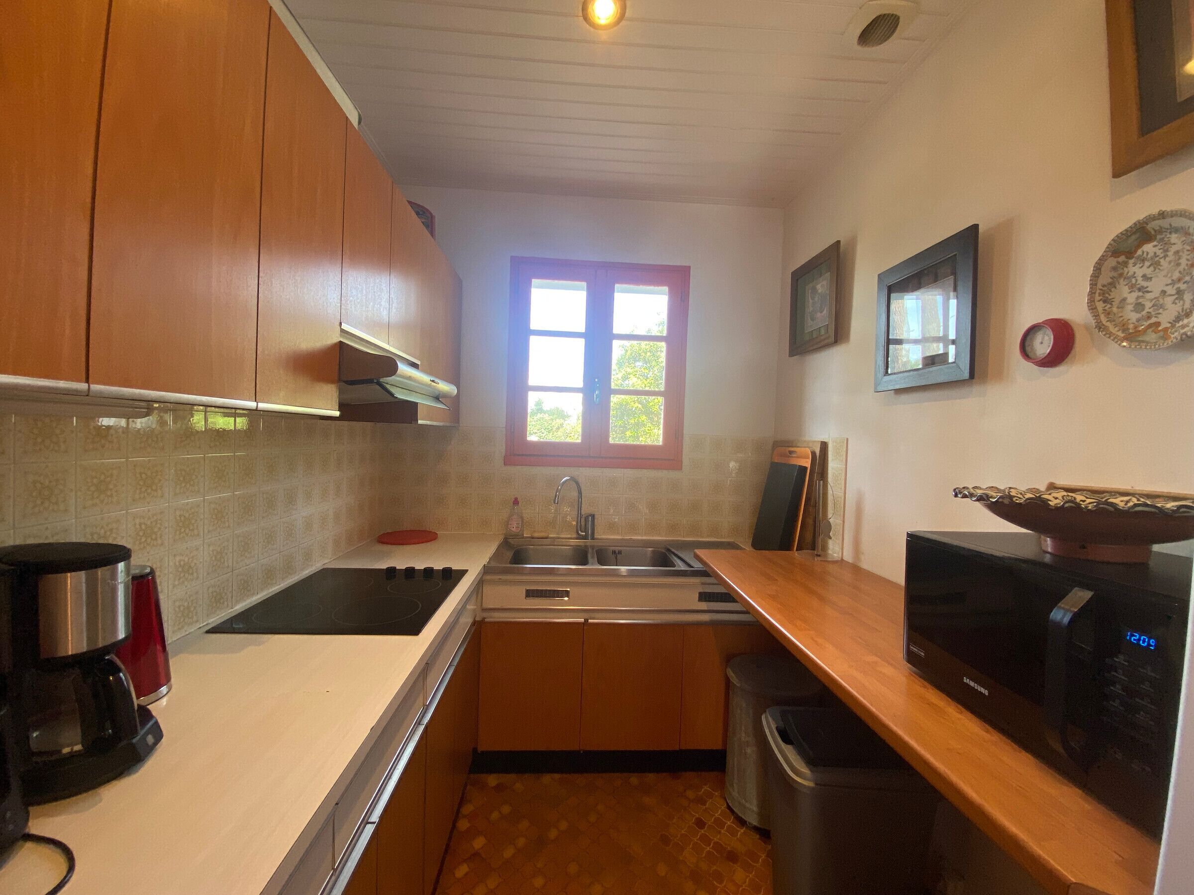 Una cocina compacta con armarios de madera, un lavamanos de acero inoxidable, un microondas y una cafetera.