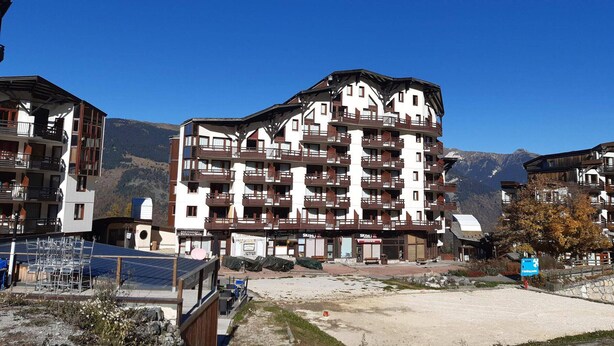 Een meerhoog hotel met balkons, een bord met ski-oord en een bergachtige achtergrond.