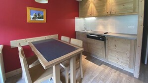 Een kleine keuken met houten kastjes, een geïntegreerde vaatwasser en een rode accentmuur.