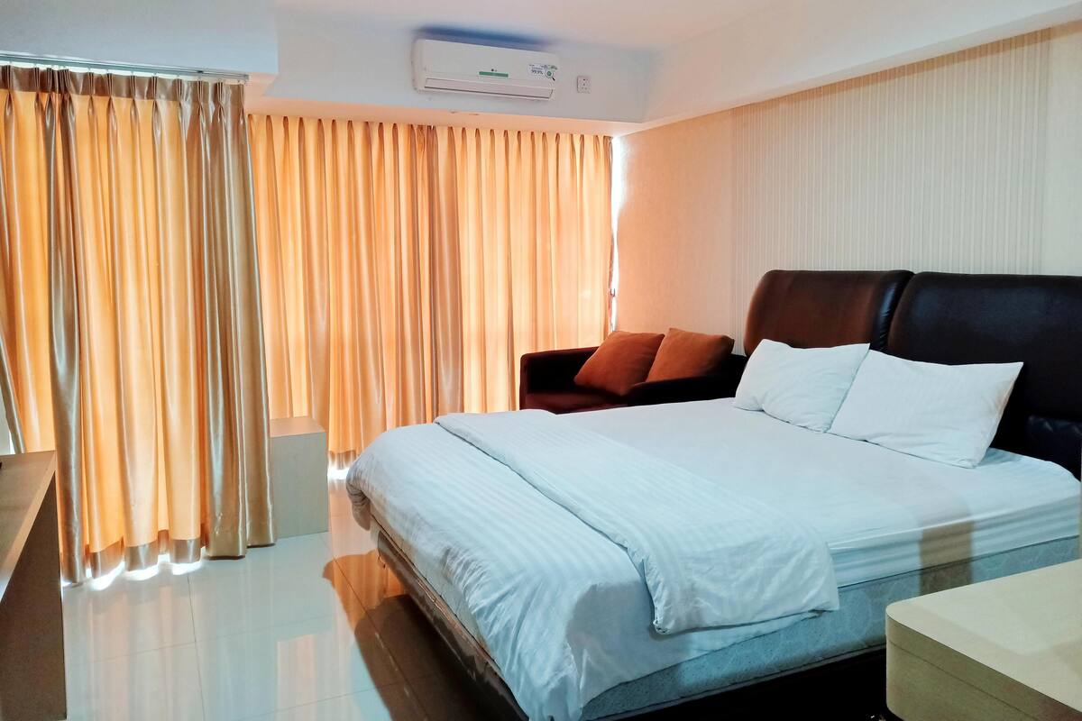 Ein Hotelzimmer mit einem großen Bett, einem Nachttisch, einem Sessel und einem Fenster mit Vorhängen.