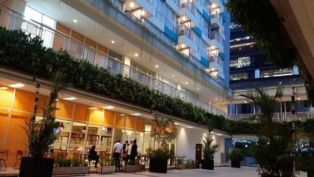 A multi-story hotel with outdoor seating areas, a covered walkway, and balconies with plants.
