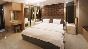 A modern hotel room with a large bed, a vanity with a mirror, and a wall-mounted headboard.