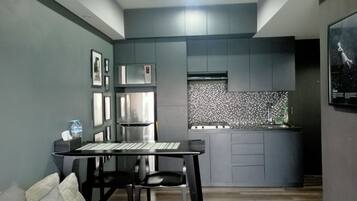 A compact kitchen with a modern design, featuring a built-in microwave, a stainless steel refrigerator, and a tiled backsplash.