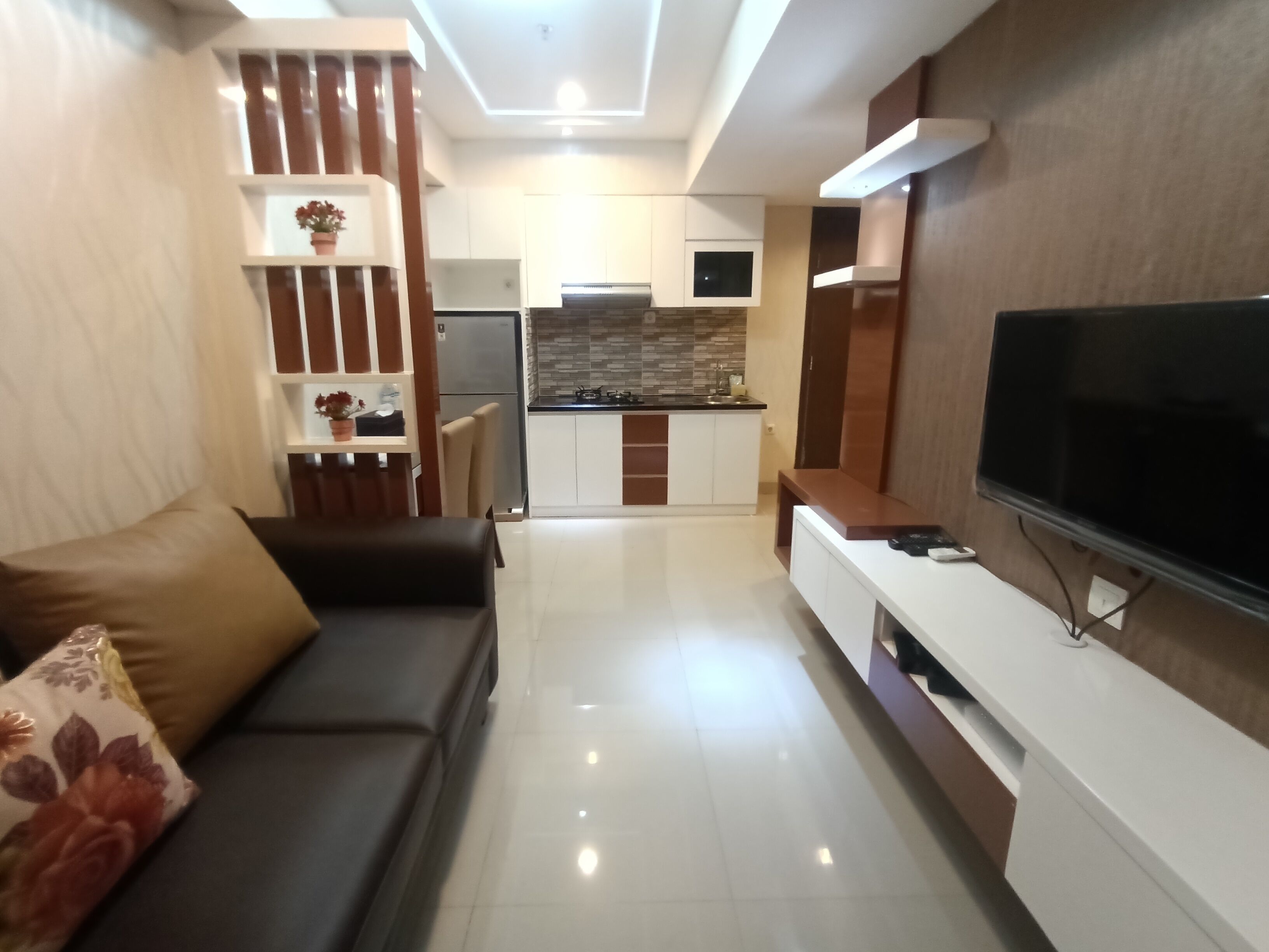 A modern living room with a sofa, a TV, and a kitchen in the background.