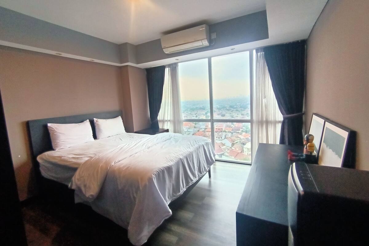 Ein Hotelzimmer mit einem Bett, einem Schreibtisch und einem großen Fenster mit Blick auf die Stadt.