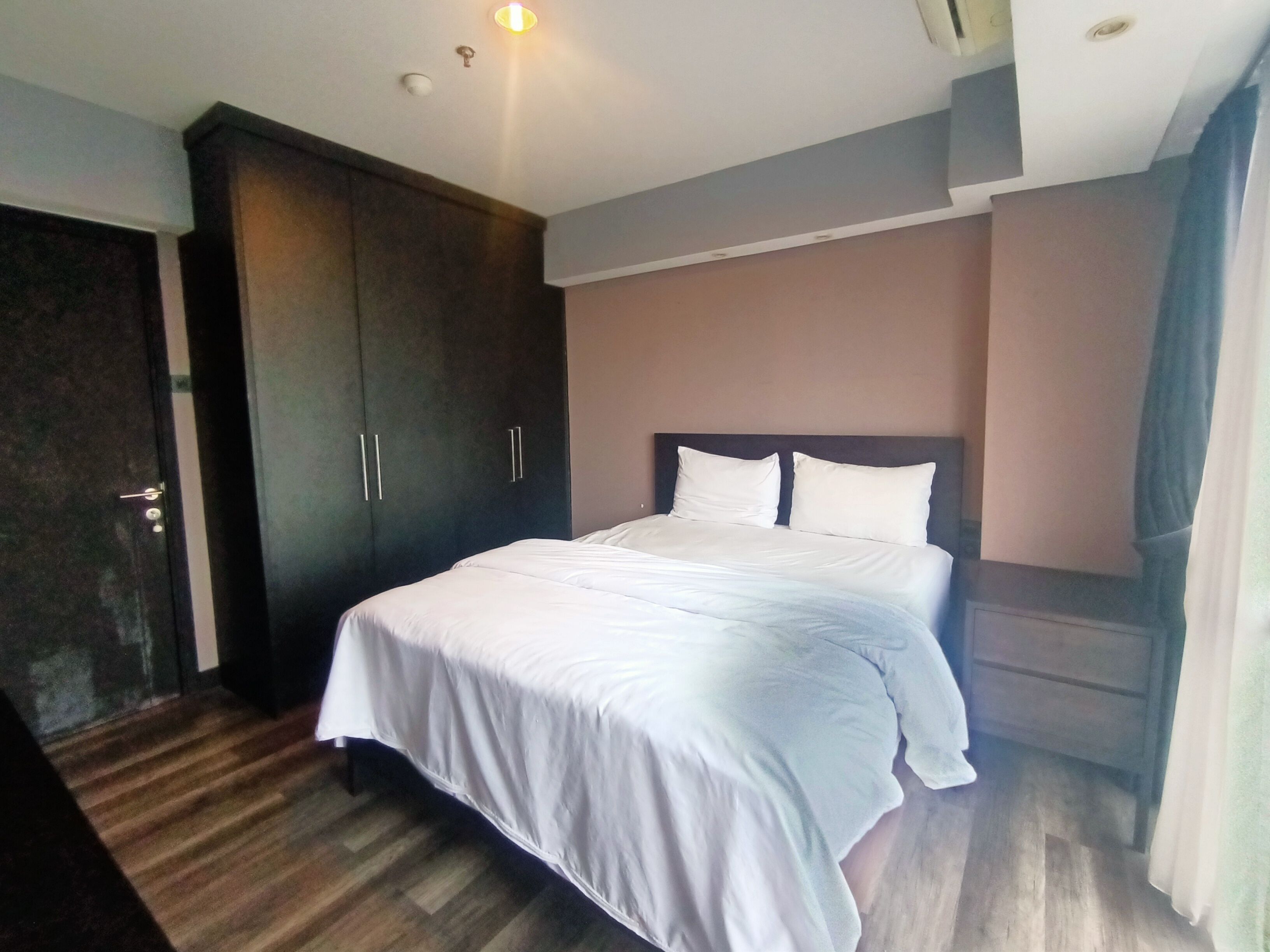 A hotel room with a large bed, a wardrobe, and a ceiling light.