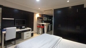 Habitación de hotel con cama, escritorio, silla, televisor, kitchenette y armario.