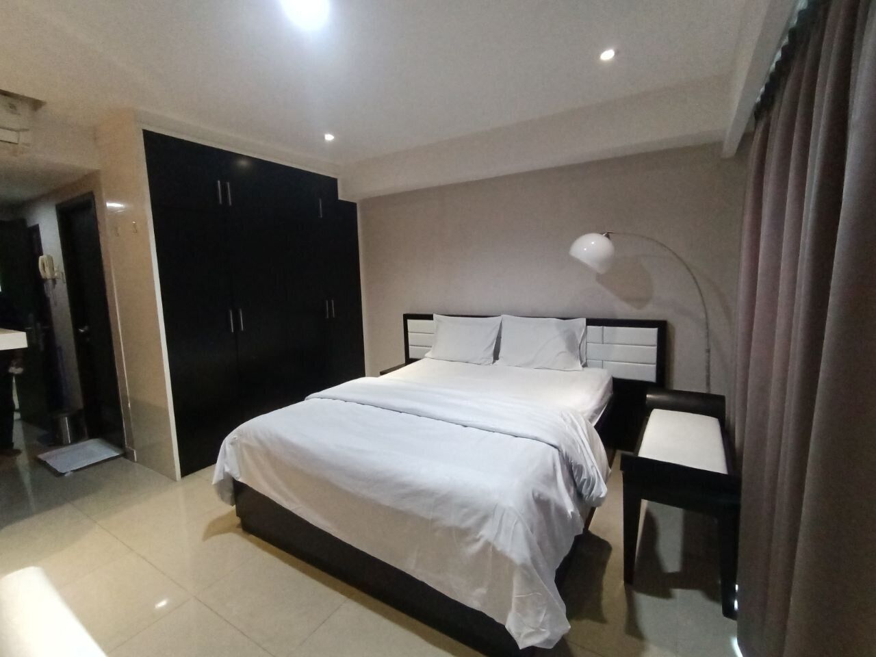 A modern hotel room with a large bed, a bedside table, and a wardrobe.