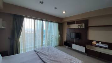 Habitación de hotel con una cama grande, un televisor de pantalla plana en la pared, un estante con una planta y una ventana con cortinas.