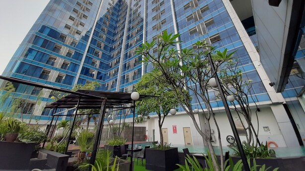 Un edificio moderno de gran altura con fachada de vidrio, zona de estar al aire libre con mesas y sillas, y áreas verdes.