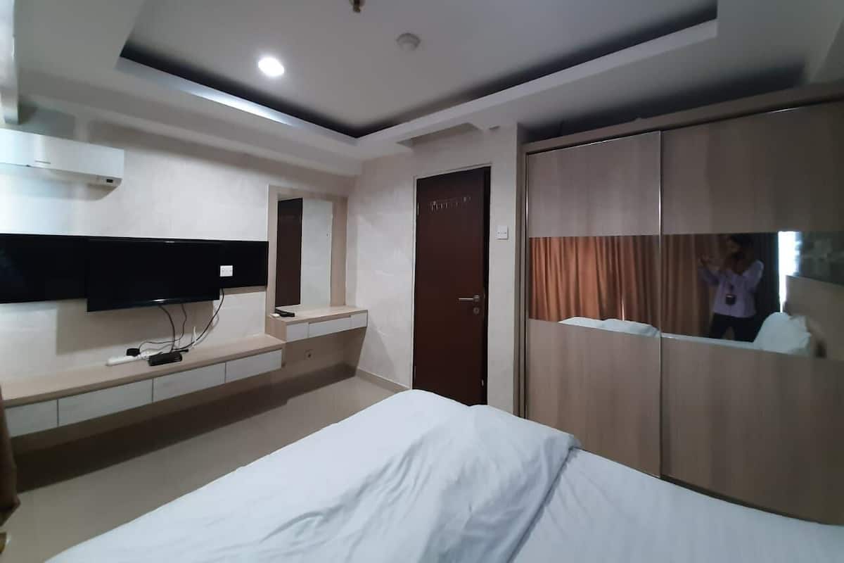 Una habitación de hotel con cama, televisor en la pared, armario y puerta.