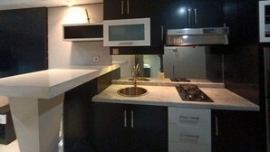 Una cocina compacta con armarios oscuros, un lavamanos de acero inoxidable, un microondas y una estufa a gas.