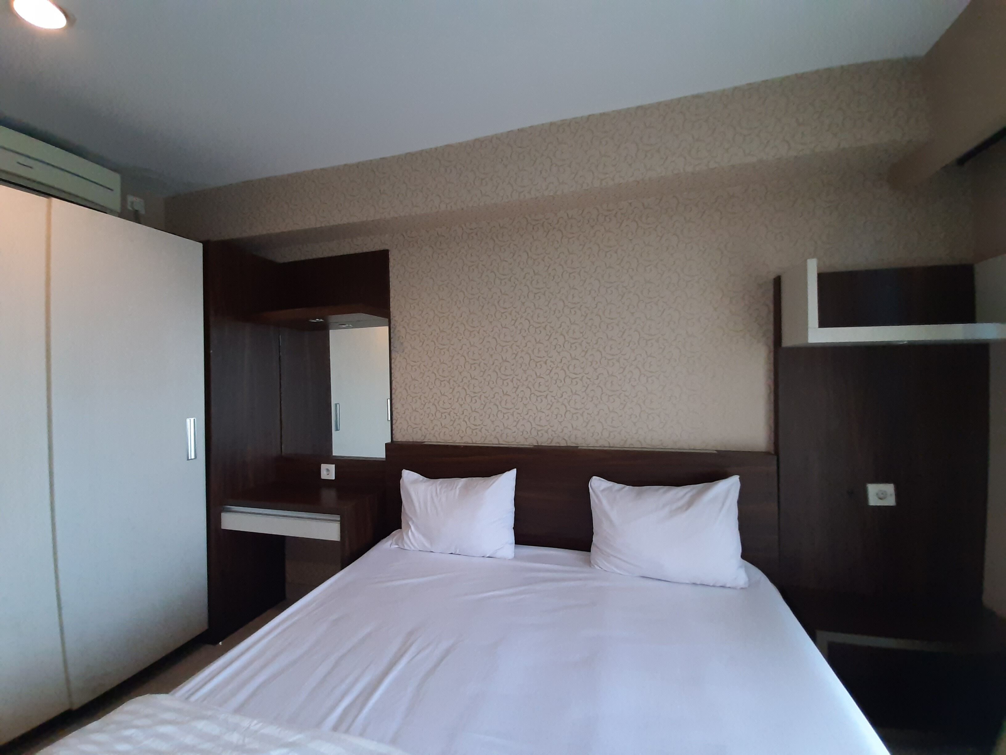 Une chambre d’hôtel avec un grand lit, une armoire, un miroir et un petit bureau.
